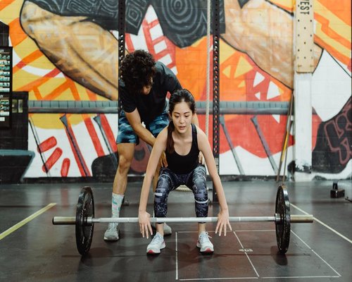 Coach explaining correct barbell technique to a fitness beginner student